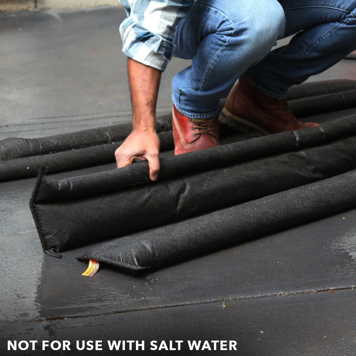 Placing Quick Dam Flood Barriers on wet ground to block water showing proper setup and warning not for use with salt water.