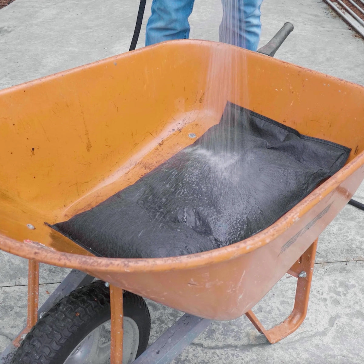 Pre-activating a Quick Dam Flood Bag in a barrel with a hose showing how the bag absorbs water and expands before flood protection use.