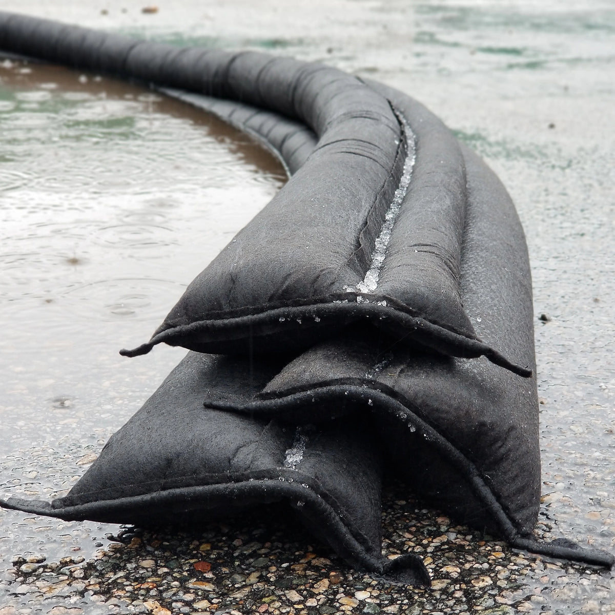 Quick Dam Flood Barriers stacked in a pyramid formation on wet ground creating a strong water activated wall to block and divert flood water.