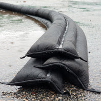 Quick Dam Flood Barriers stacked in a pyramid formation on wet ground creating a strong water activated wall to block and divert flood water.