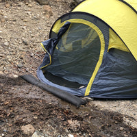 Quick Dam Flood Barrier placed in front of a yellow camping tent entrance blocking rainwater runoff and keeping the inside dry.