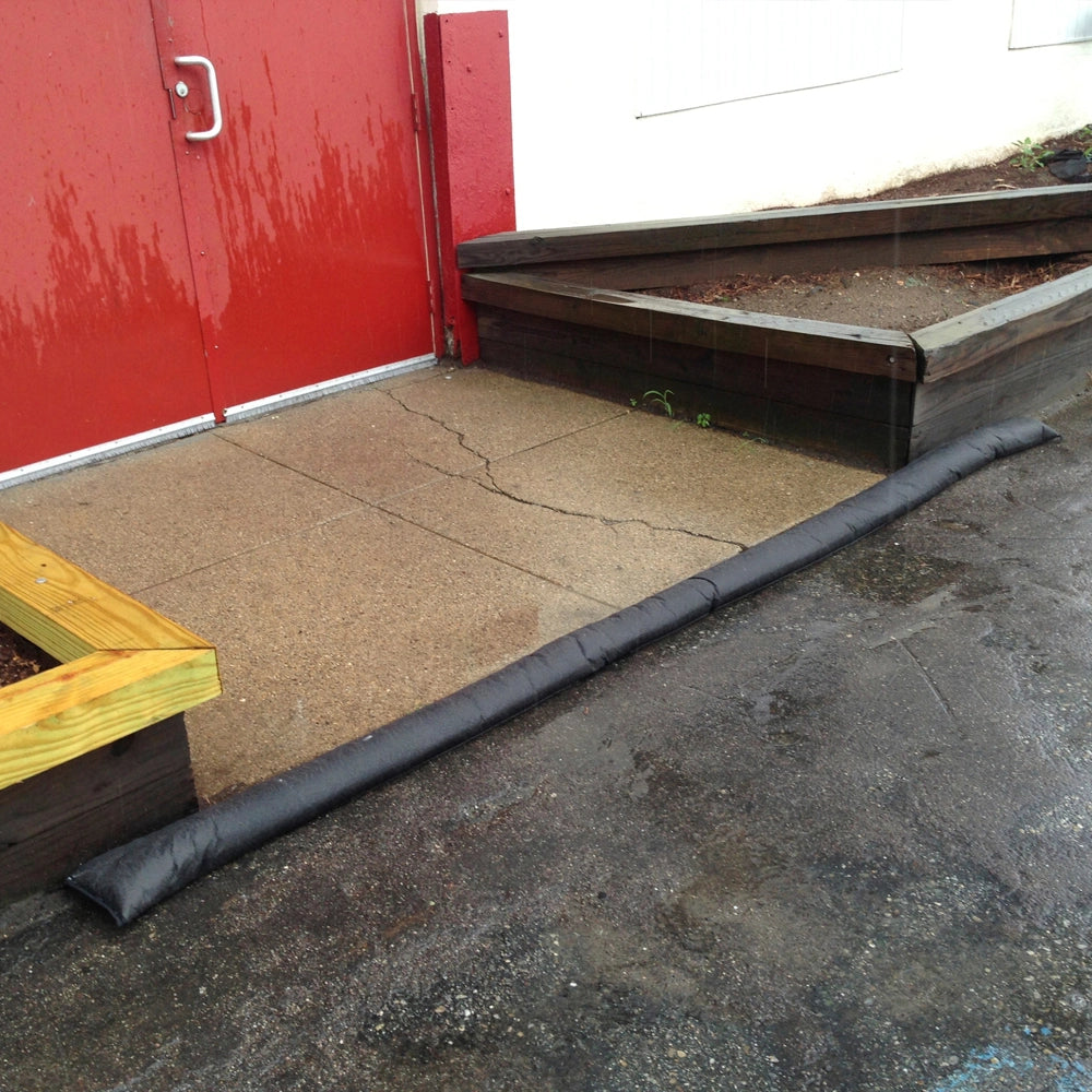 Quick Dam Flood Barrier placed in front of a red door on wet pavement protecting a building entrance from rainwater and flooding.