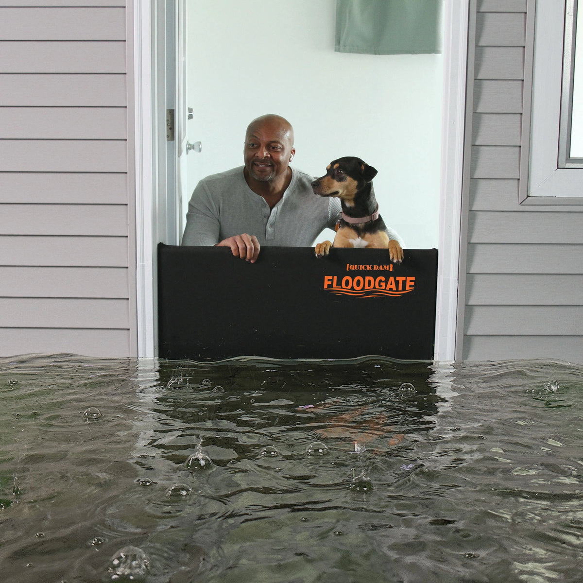 Man and dog standing safely behind a Quick Dam Flood Gate at a doorway with rising flood water outside showing strong home flood protection.