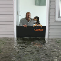 Man and dog standing safely behind a Quick Dam Flood Gate at a doorway with rising flood water outside showing strong home flood protection.