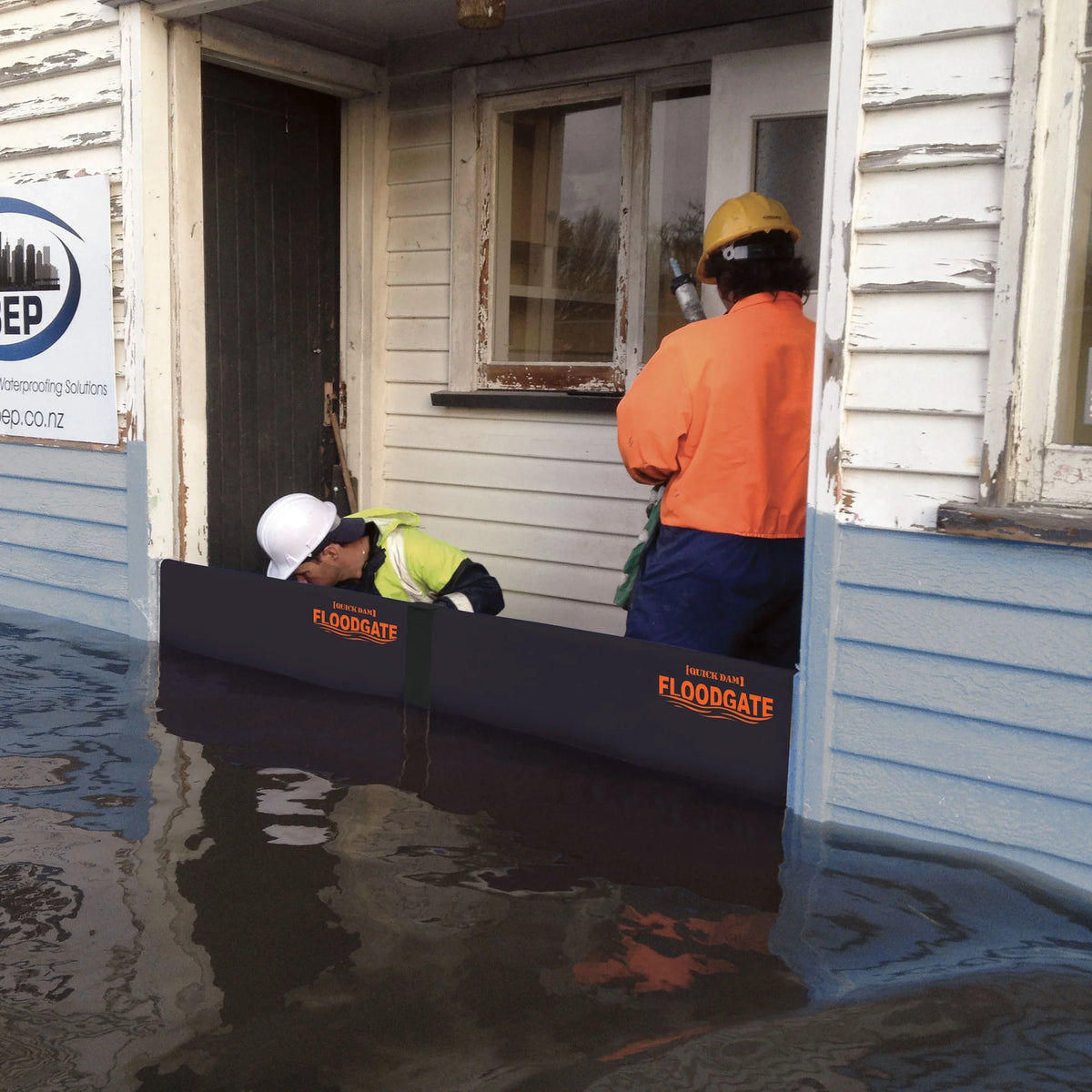 Workers install Quick Dam Flood Gates at a flooded building entrance, creating a strong barrier to block rising water.