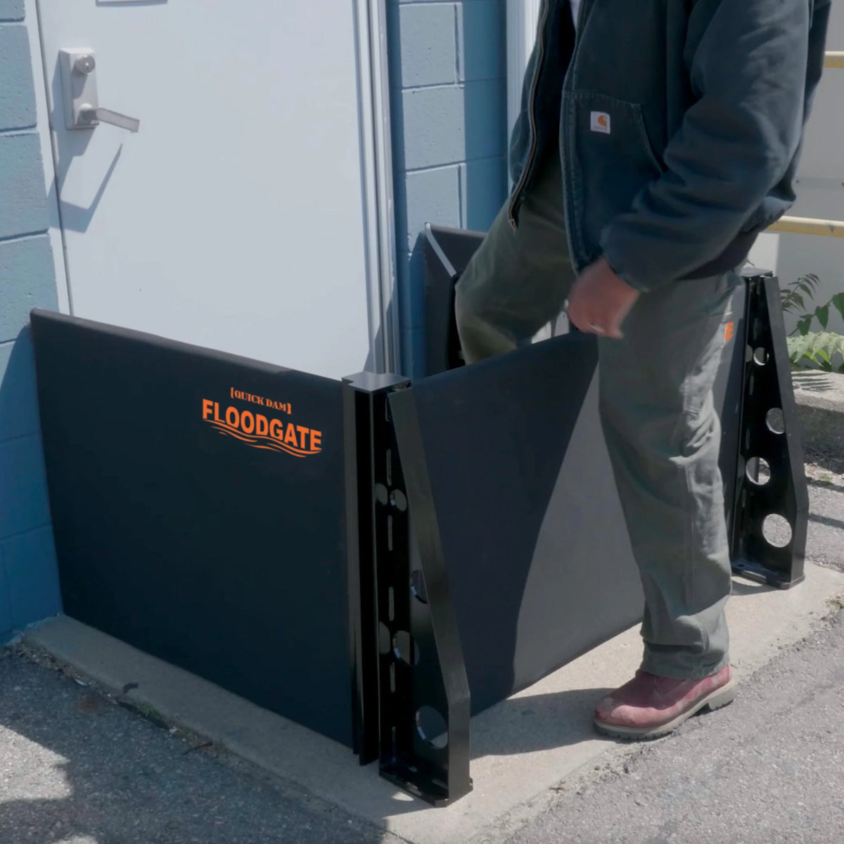 Quick Dam Flood Gate with stanchions installed at a doorway as a person steps over the barrier, demonstrating flood protection setup.