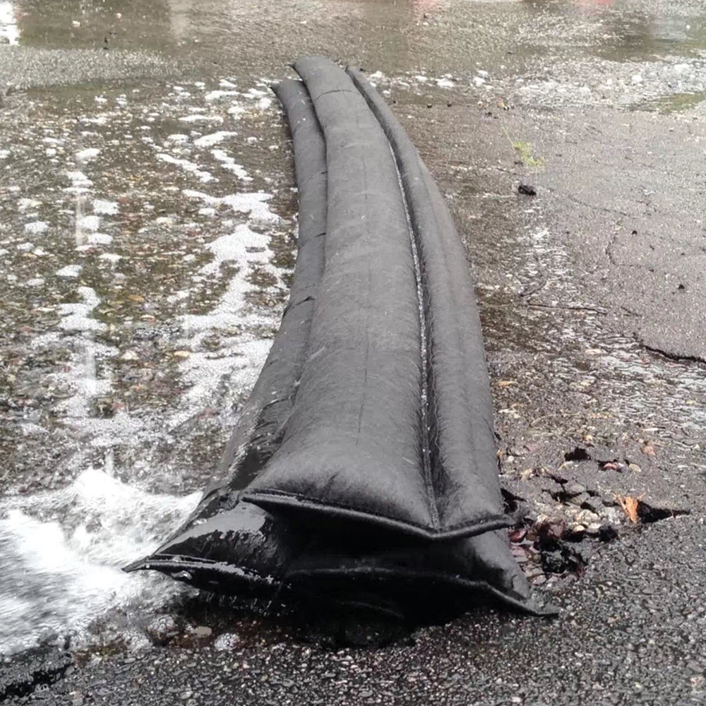 Quick Dam Flood Barriers stacked to block and divert rushing water on pavement, providing fast flood protection and water damage prevention.