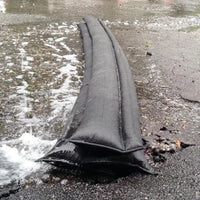 Quick Dam Flood Barriers stacked to block and divert rushing water on pavement, providing fast flood protection and water damage prevention.