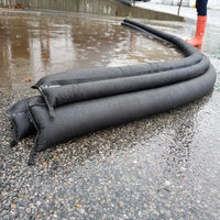 Quick Dam Flood Barriers stacked in layers and curved along pavement, effectively blocking rising rainwater and providing strong flood protection.