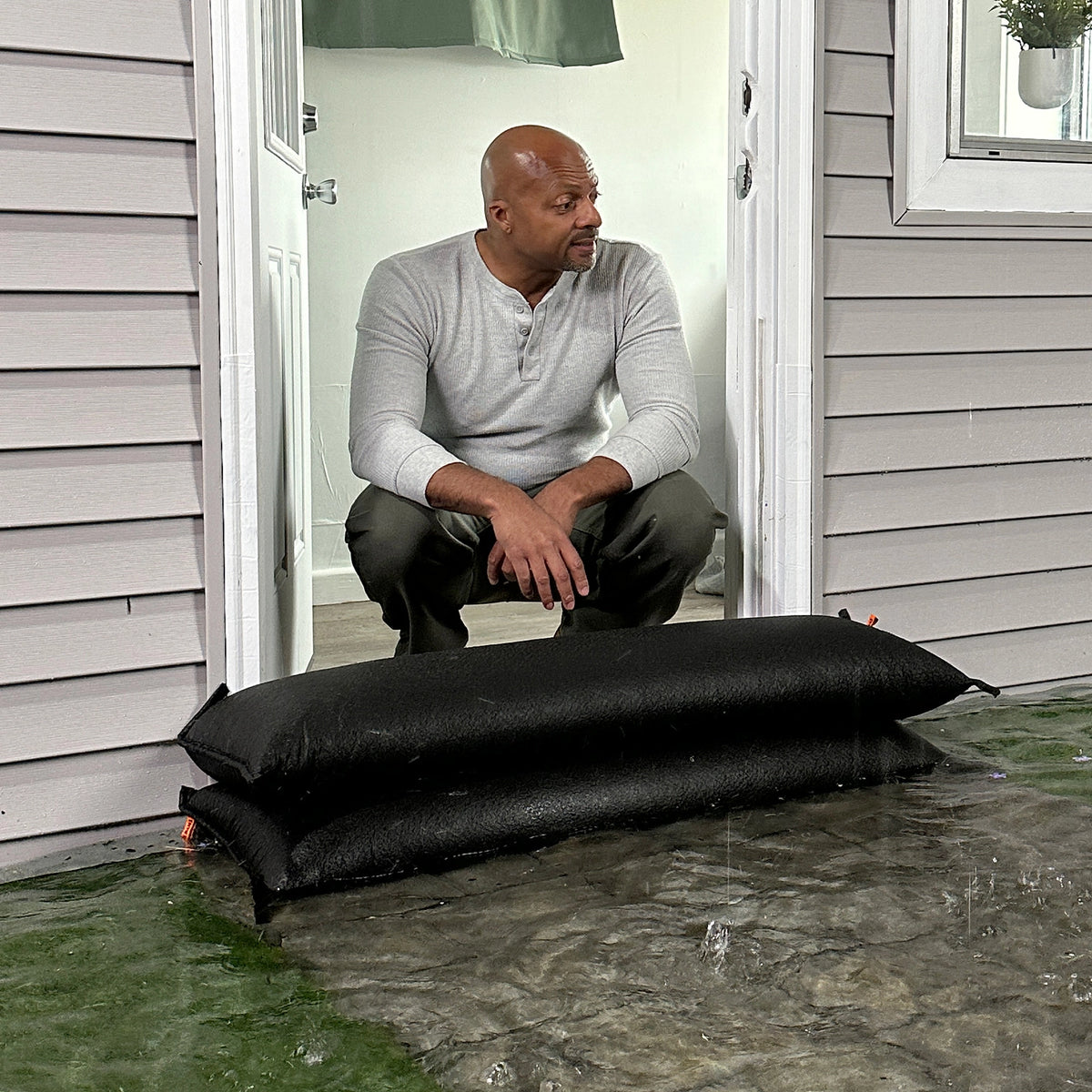 Homeowner using stacked Quick Dam Flood Bags at doorway to block rising floodwater and protect interior.