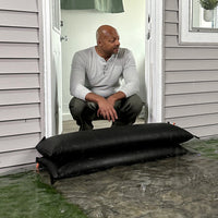 Homeowner using stacked Quick Dam Flood Bags at doorway to block rising floodwater and protect interior.