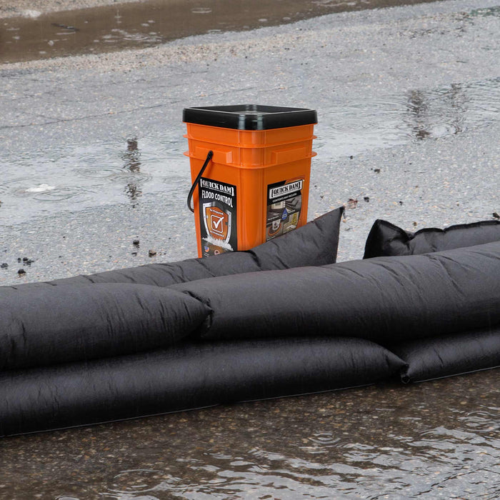 Quick Dam Outdoor Grab & Go Bucket Kit with black water-activated flood barriers deployed on wet pavement, providing portable flood protection.