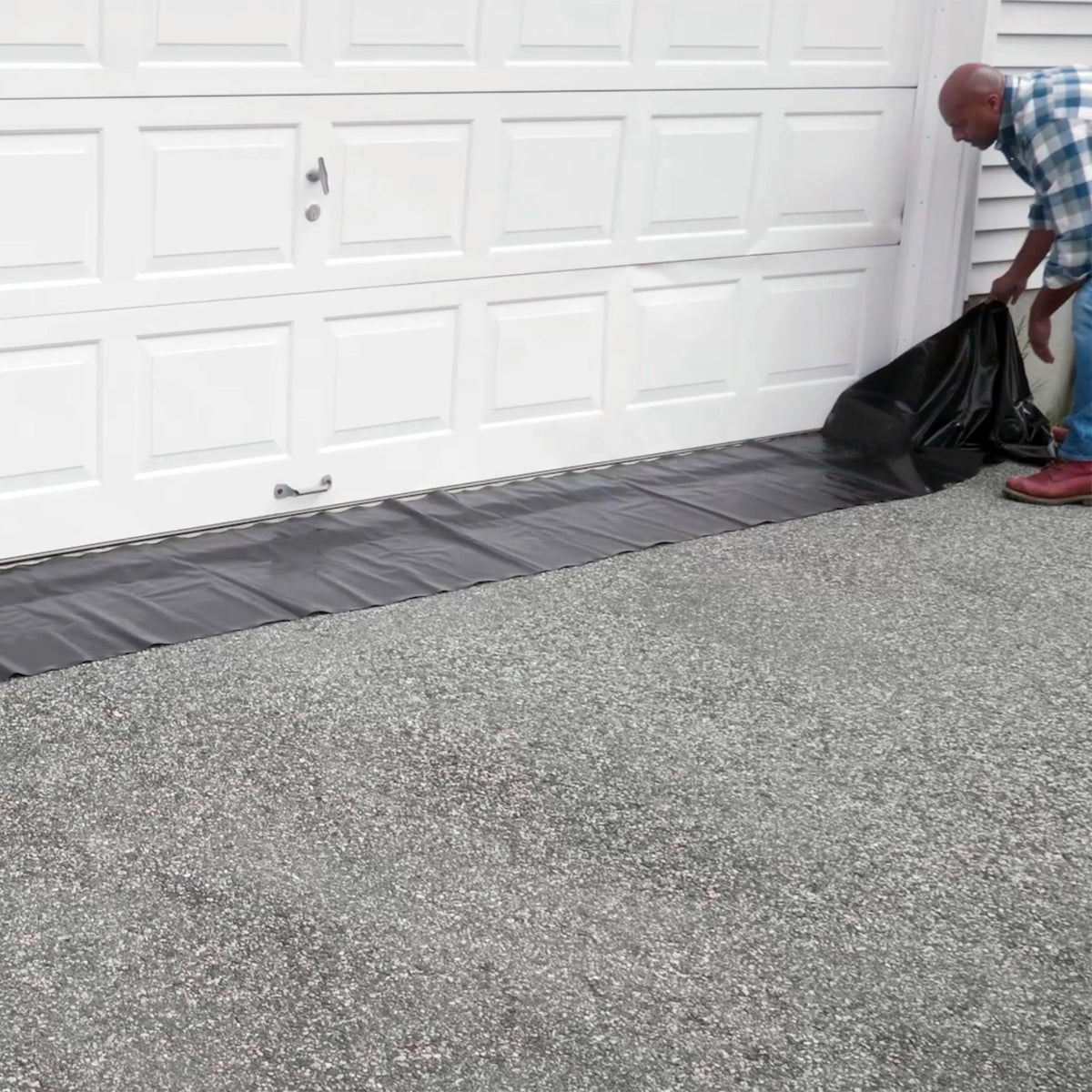 Man setting up a Quick Dam Water Curb in front of a garage door to block floodwater, showing easy placement along the driveway.
