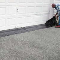 Man setting up a Quick Dam Water Curb in front of a garage door to block floodwater, showing easy placement along the driveway.