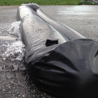 Close-up of a Quick Dam Water Curb filled with water, blocking and diverting rushing floodwater on pavement.