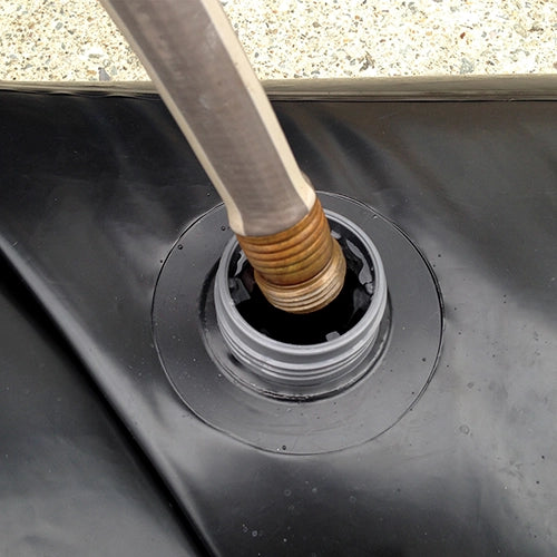 Close-up of a garden hose filling a Quick Dam Water Curb through its screw-top opening, showing easy setup for flood protection.