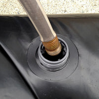 Close-up of a garden hose filling a Quick Dam Water Curb through its screw-top opening, showing easy setup for flood protection.