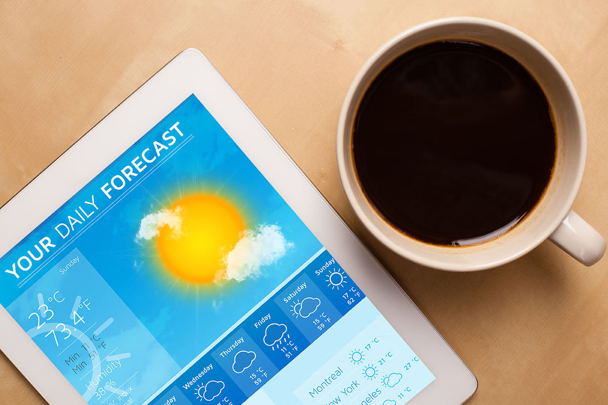 Tablet displaying a weather forecast next to a cup of coffee on a wooden surface