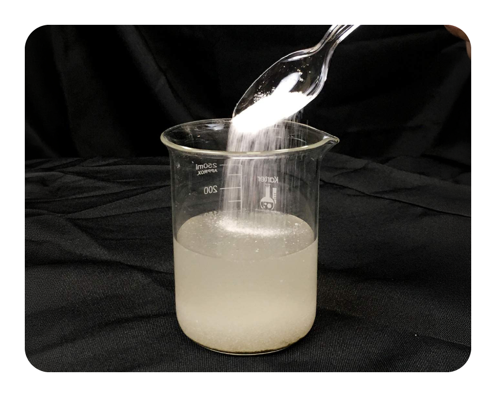 Beaker with liquid being stirred with a spoon against a black background