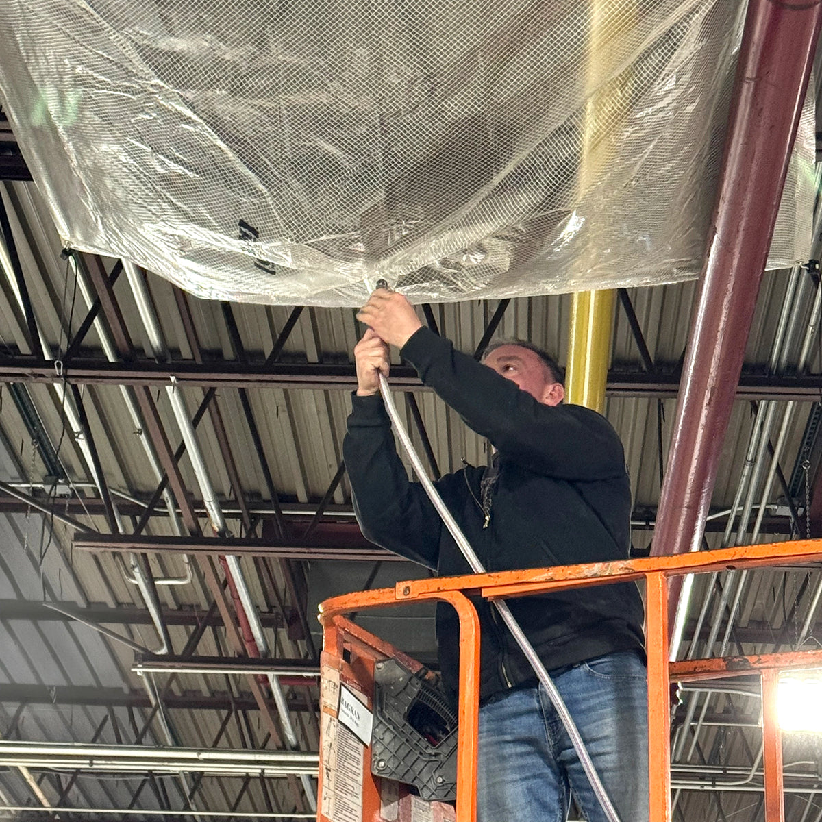 Person on a lift hanging a Quick Dam Leak Diverter in an industrial setting