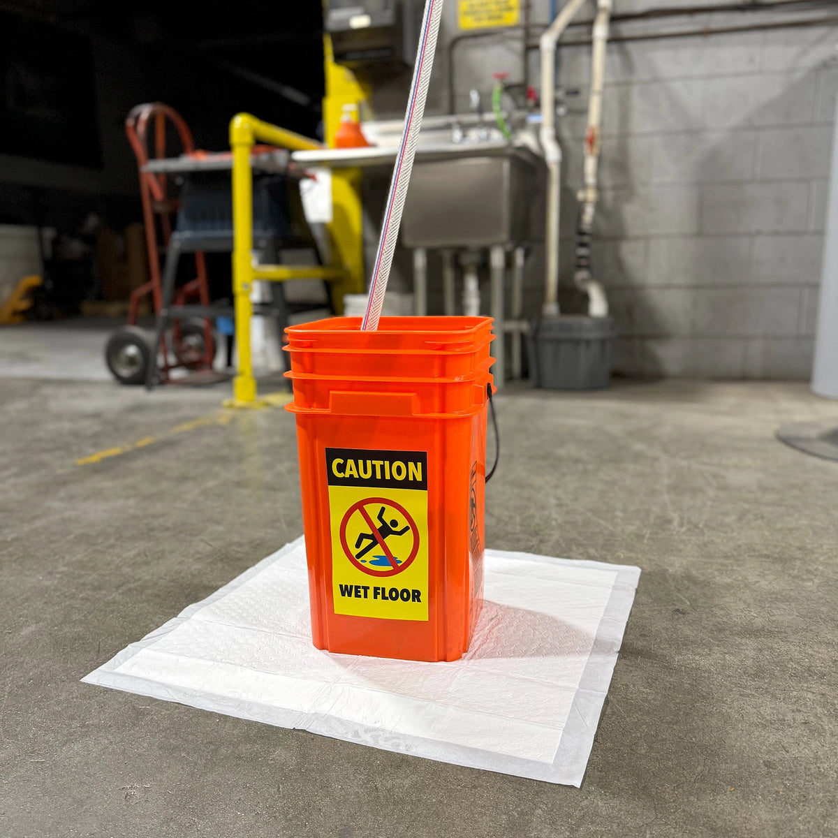 Orange Quick Dam bucket with a 'Caution: Wet Floor' sign on a concrete floor.