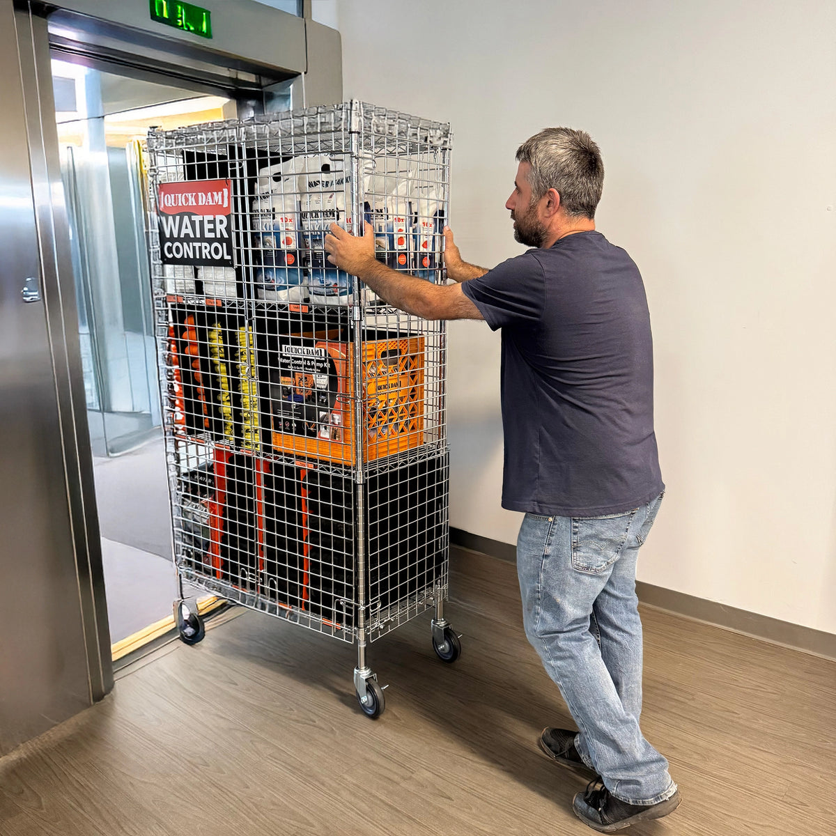 Man pushing a wire cart with flood control equipment through a door.