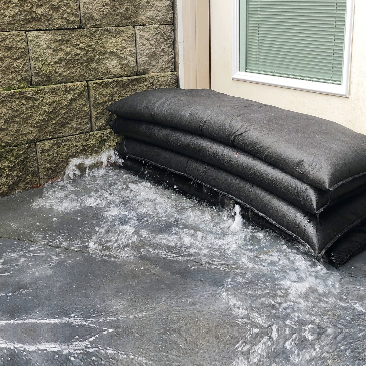Stack of black jumbo flood bags on a stone pavement next to a home