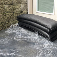 Stack of black jumbo flood bags on a stone pavement next to a home
