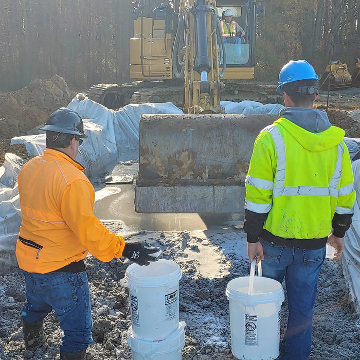 Two workers in high-visibility clothing near an excavator at a construction site.