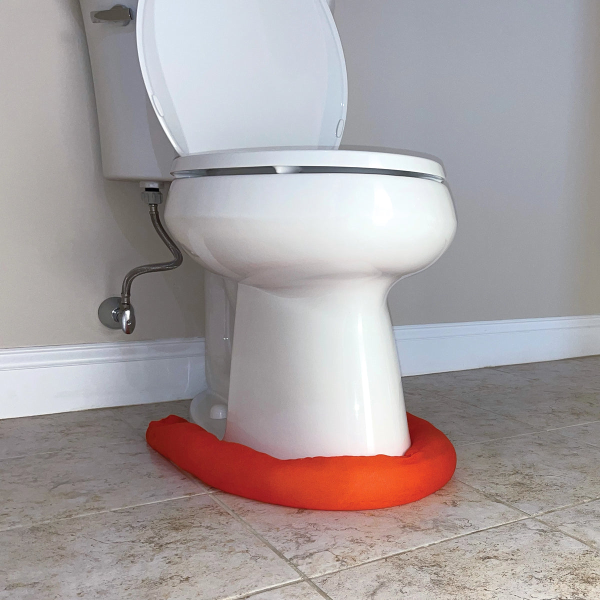 Toilet with an orange water dam on a tiled bathroom floor.