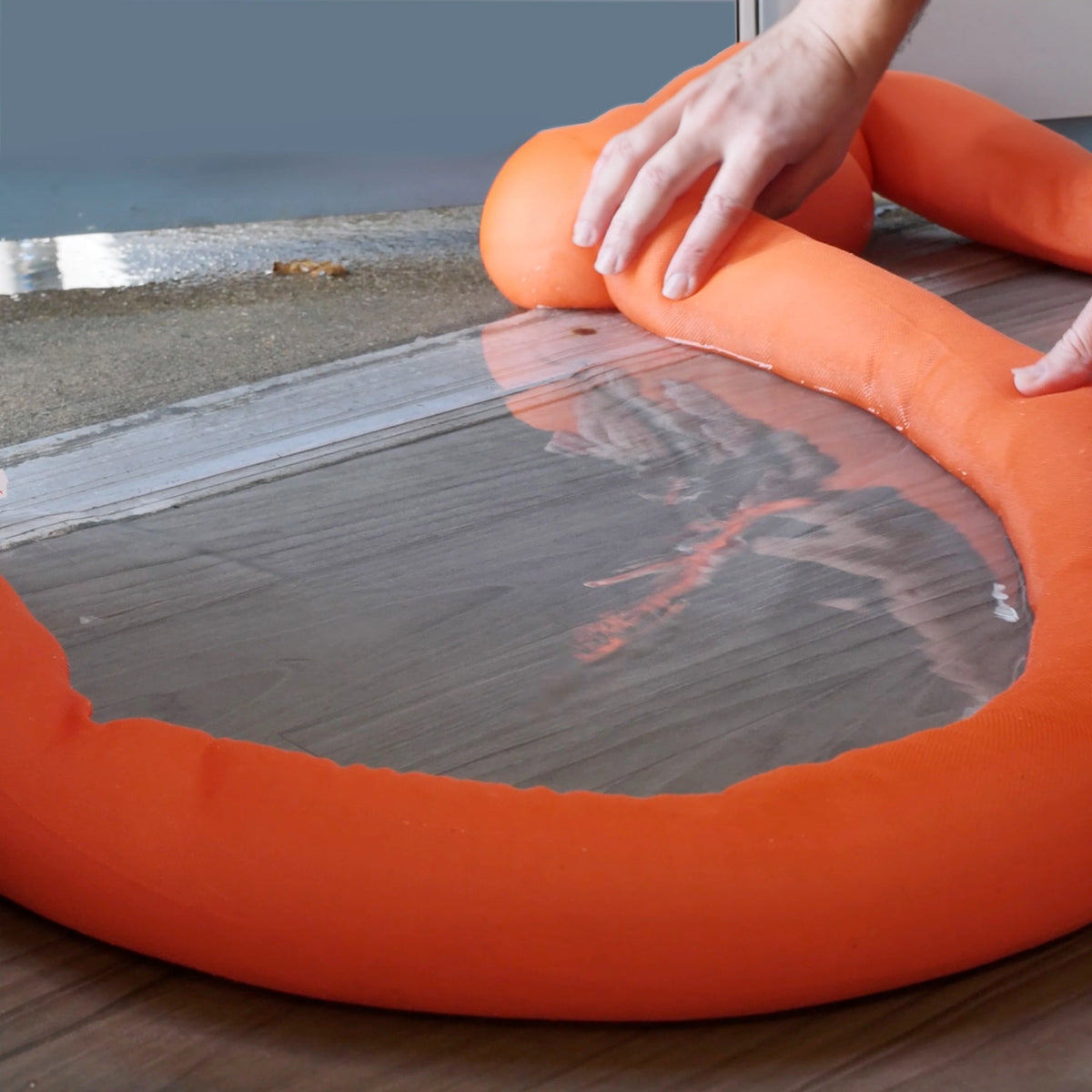 Orange water dam with a person's hand on a wooden floor.