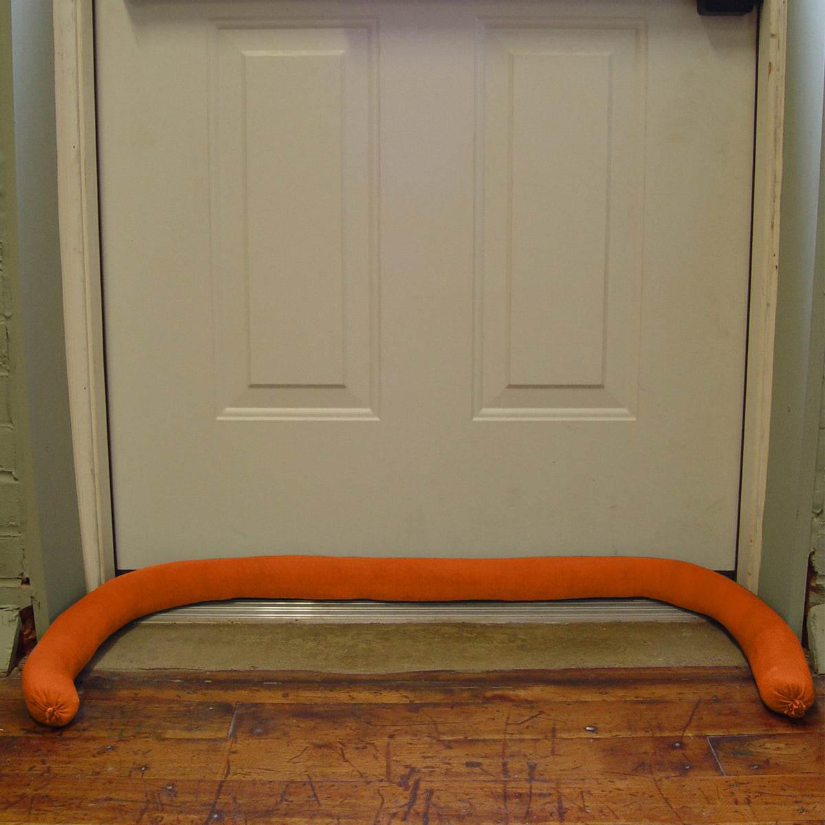 Orange water dam on a wooden floor in front of a white door.