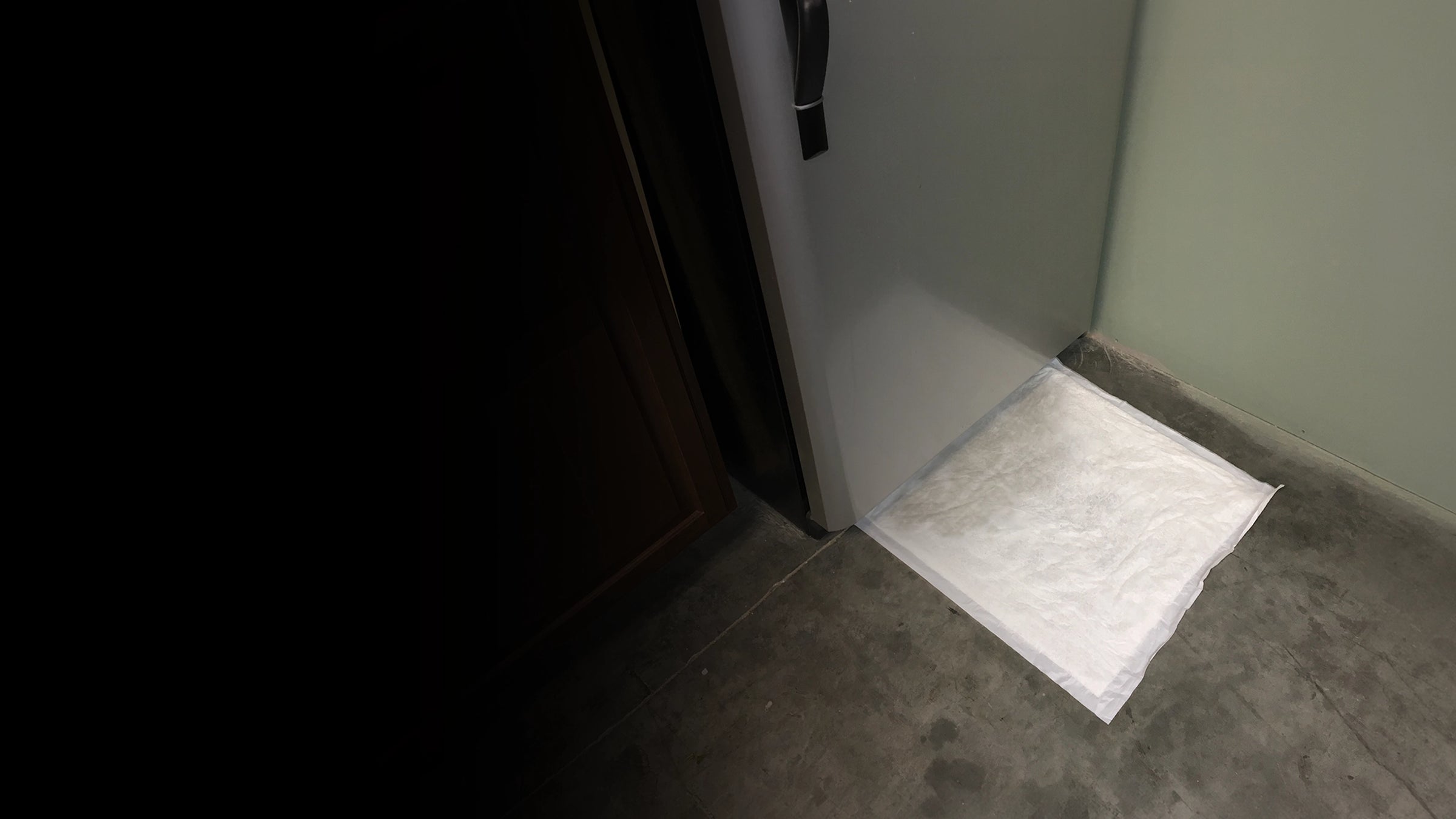 White drip mat on a gray floor next to a fridge door