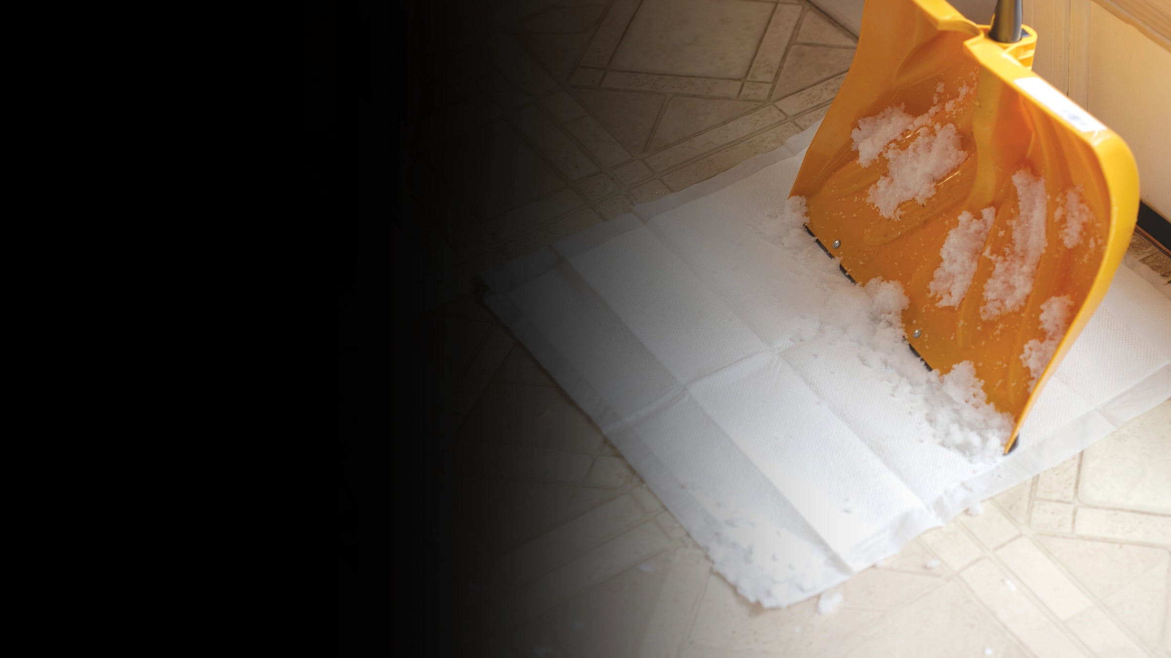 Yellow snow shovel with snow on a tiled floor