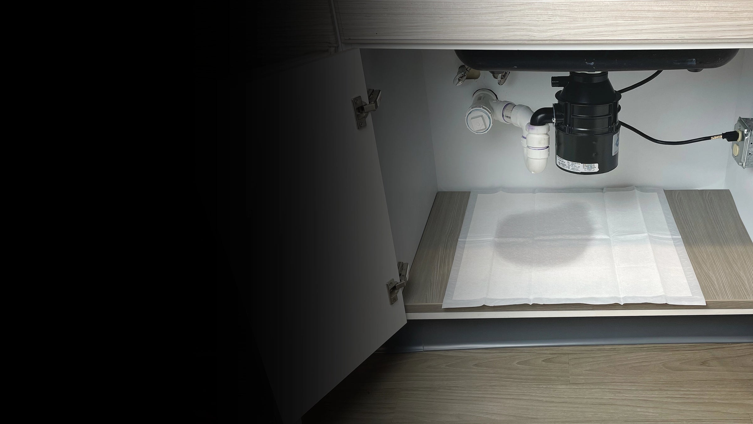 Under-cabinet water system with a pump and hoses inside an open kitchen cabinet.