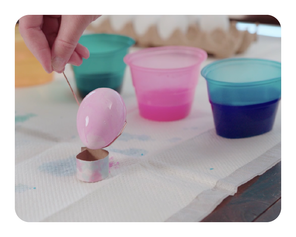 Person painting a pink egg with colorful cups in the background on a quick dam drip mat