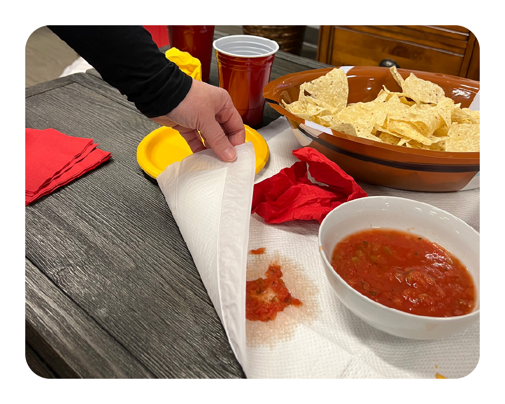 Person making a burrito with tortilla chips and salsa on a table being protected by a quick dam drip mat