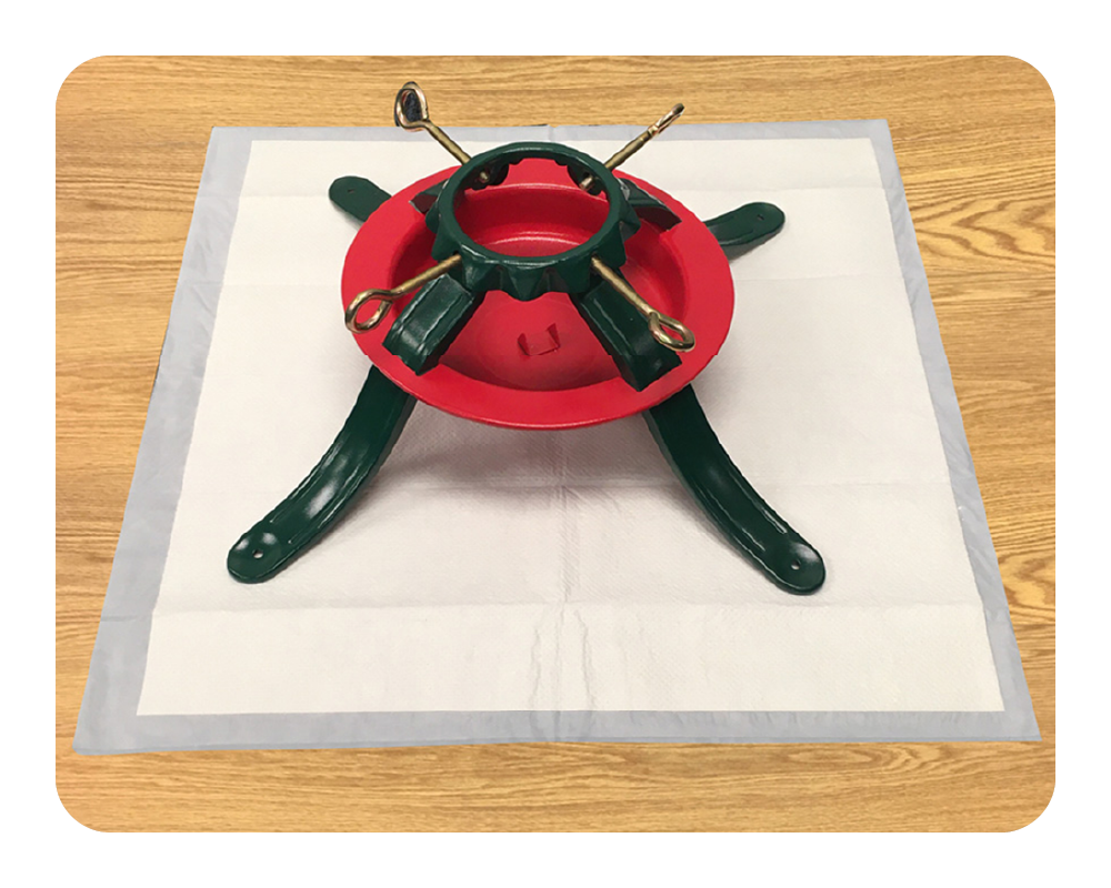 Red and green metal tree stand on a white drip mat protecting a wood floor