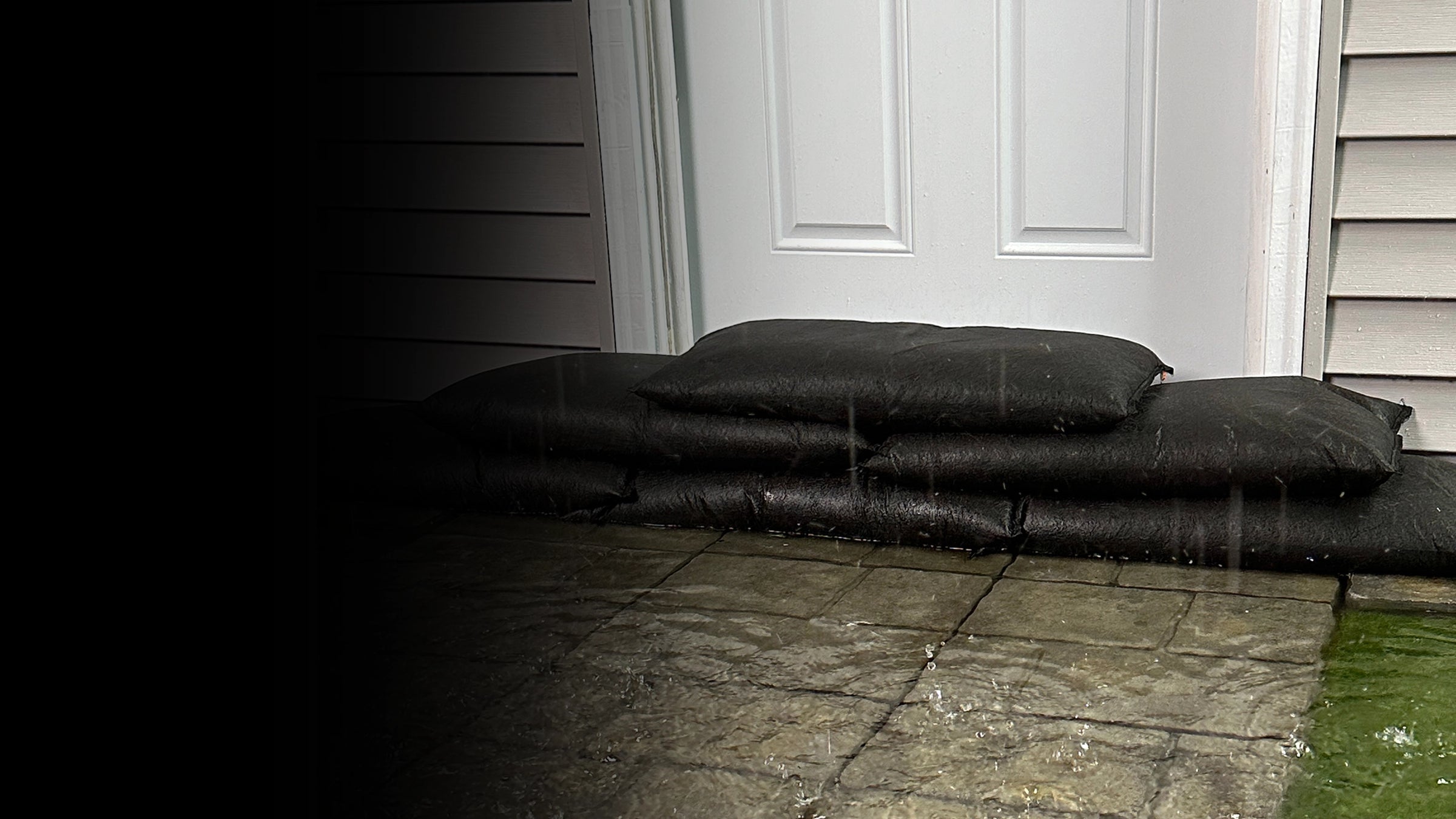 Three black flood bags stacked against a house door on a stone patio.