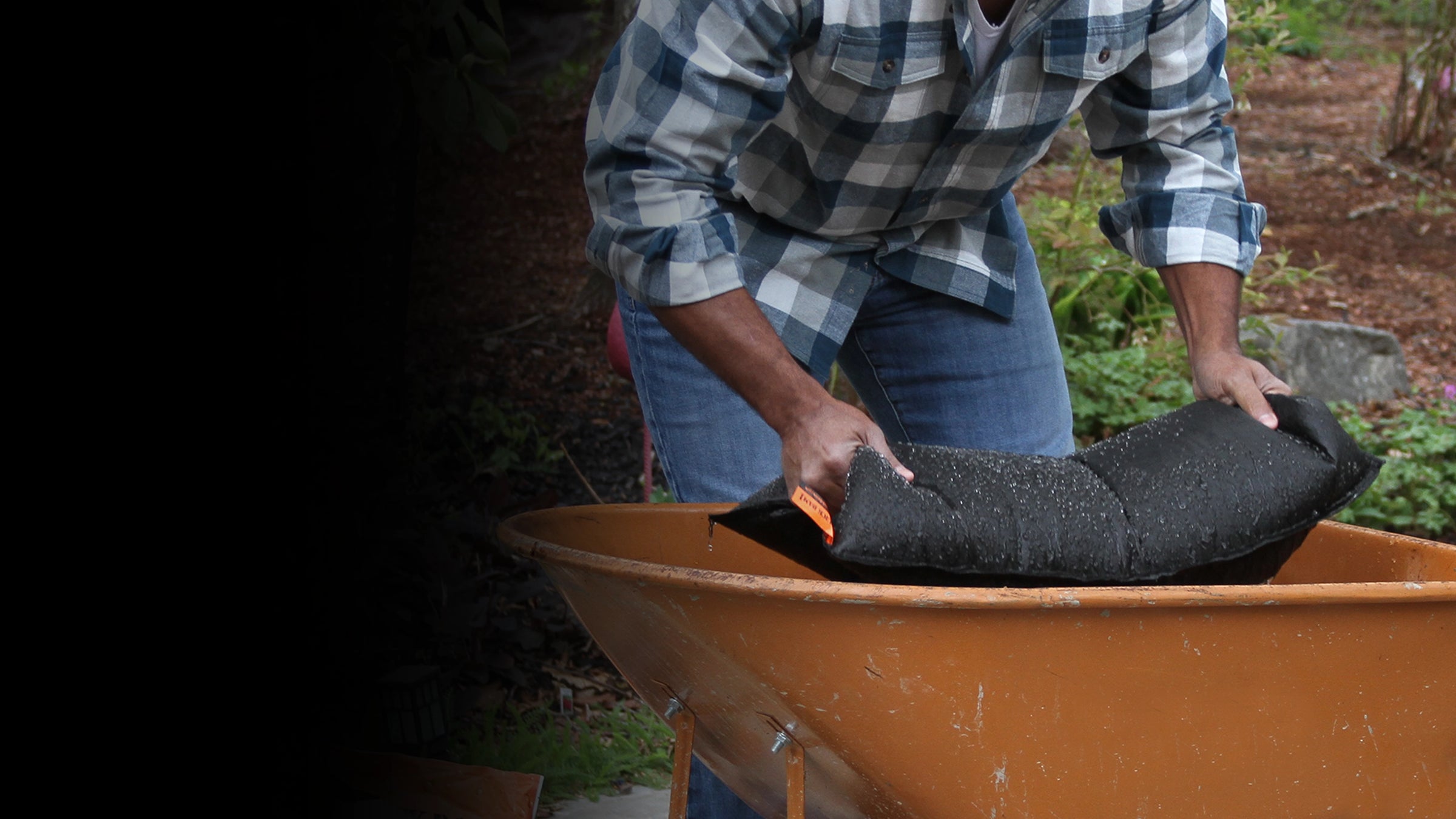 Person loading a wheelbarrow with a black flood bag outdoors