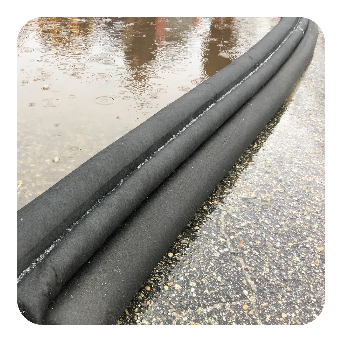 Two black flood barriers lying on wet pavement holding back flood water