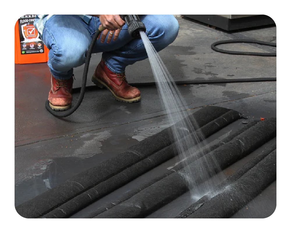 Person applying a water to rolled-out flood barriers on a flat surface