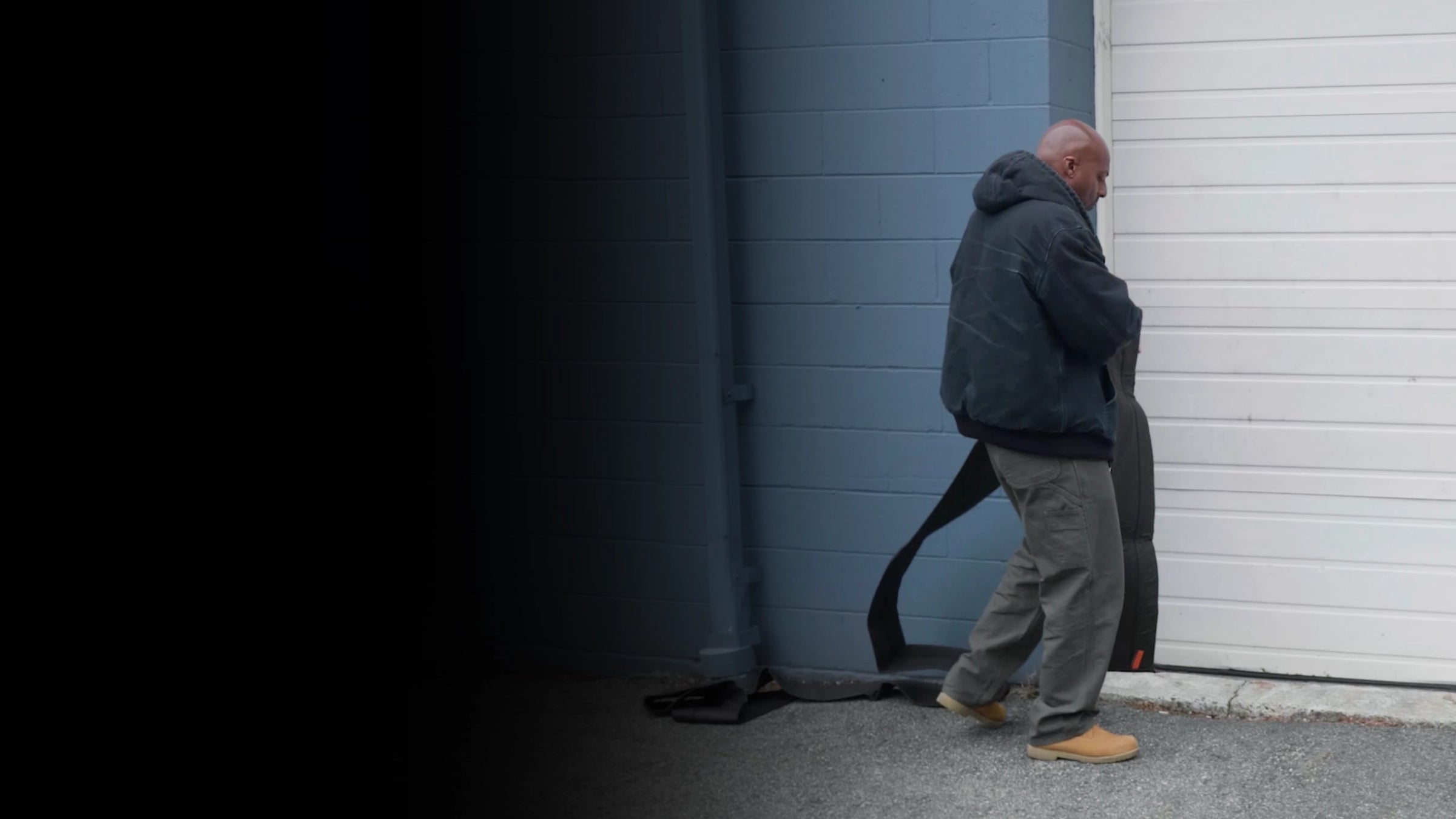 Person in dark clothing standing next to a closed garage door deploying a flood barrier