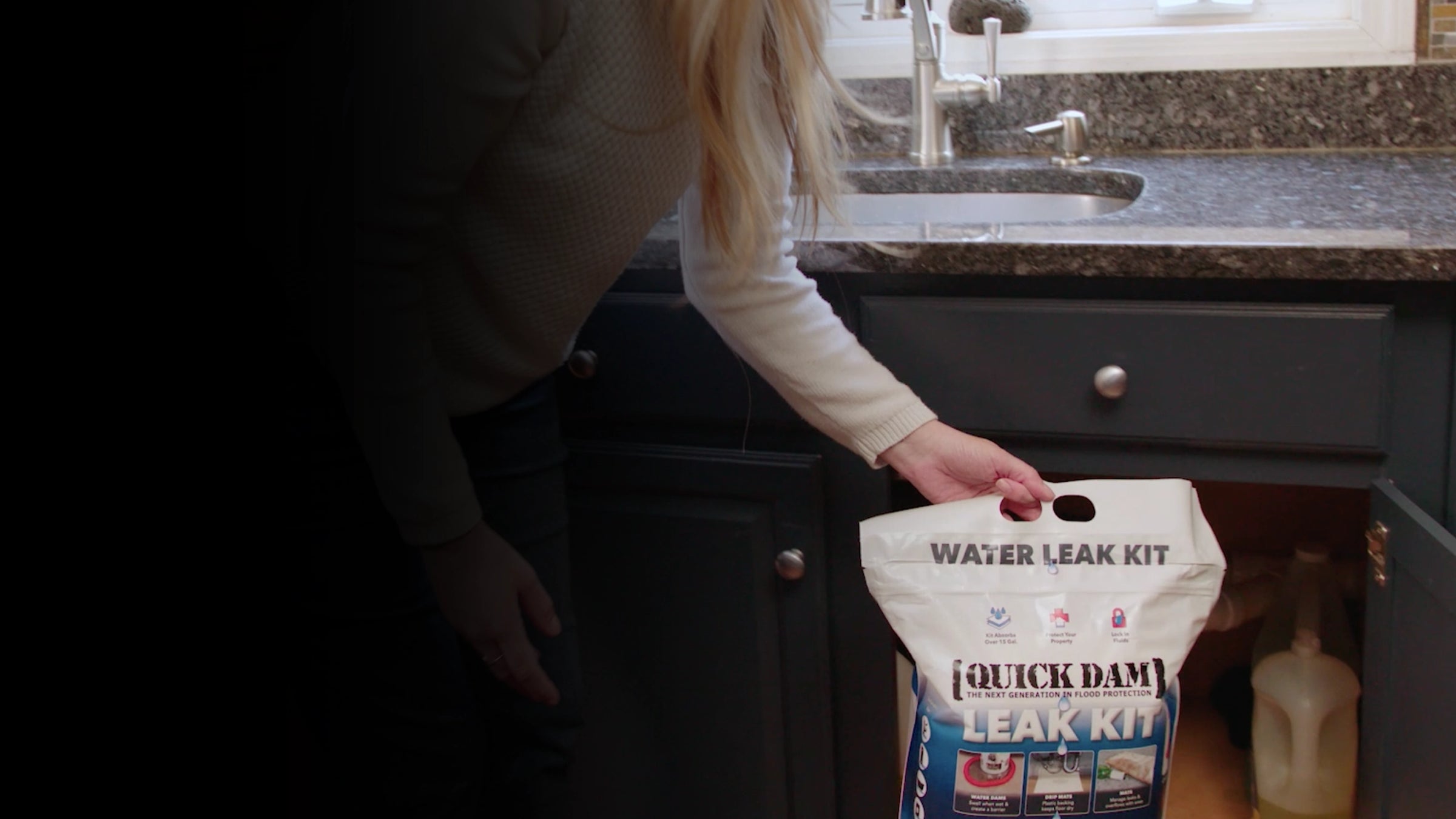 Person holding a Quick Dam water leak kit in a kitchen setting