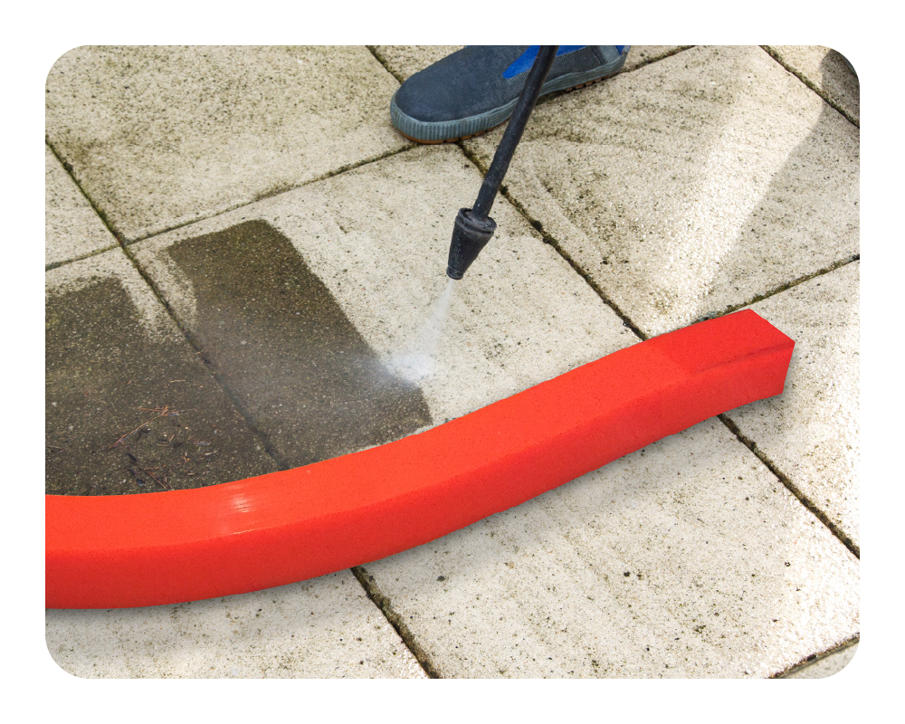 Orange insta-dam with pressure washer being used on a concrete surface with water spraying.