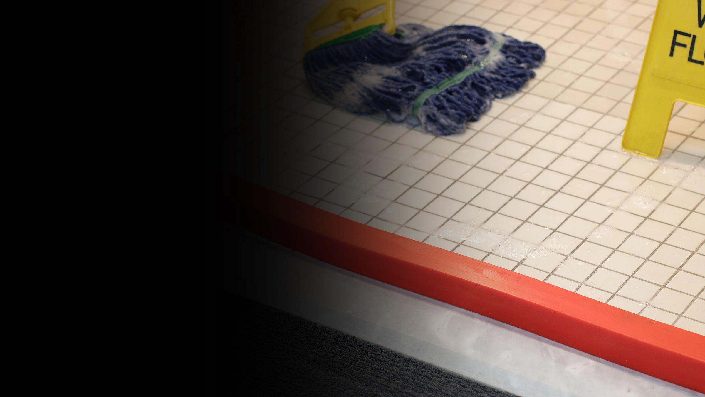 Mop on a tiled floor with an orange insta-dam and a yellow caution sign.