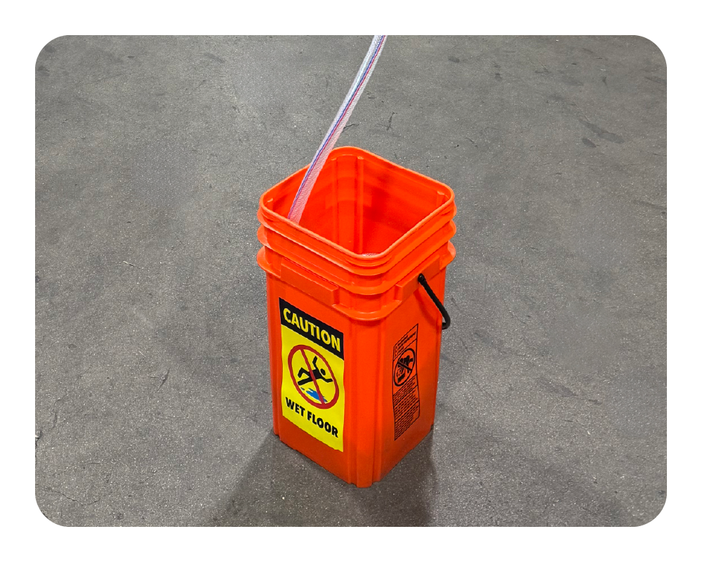 Orange bucket with a 'Caution: Wet Floor' sign on a gray concrete floor.