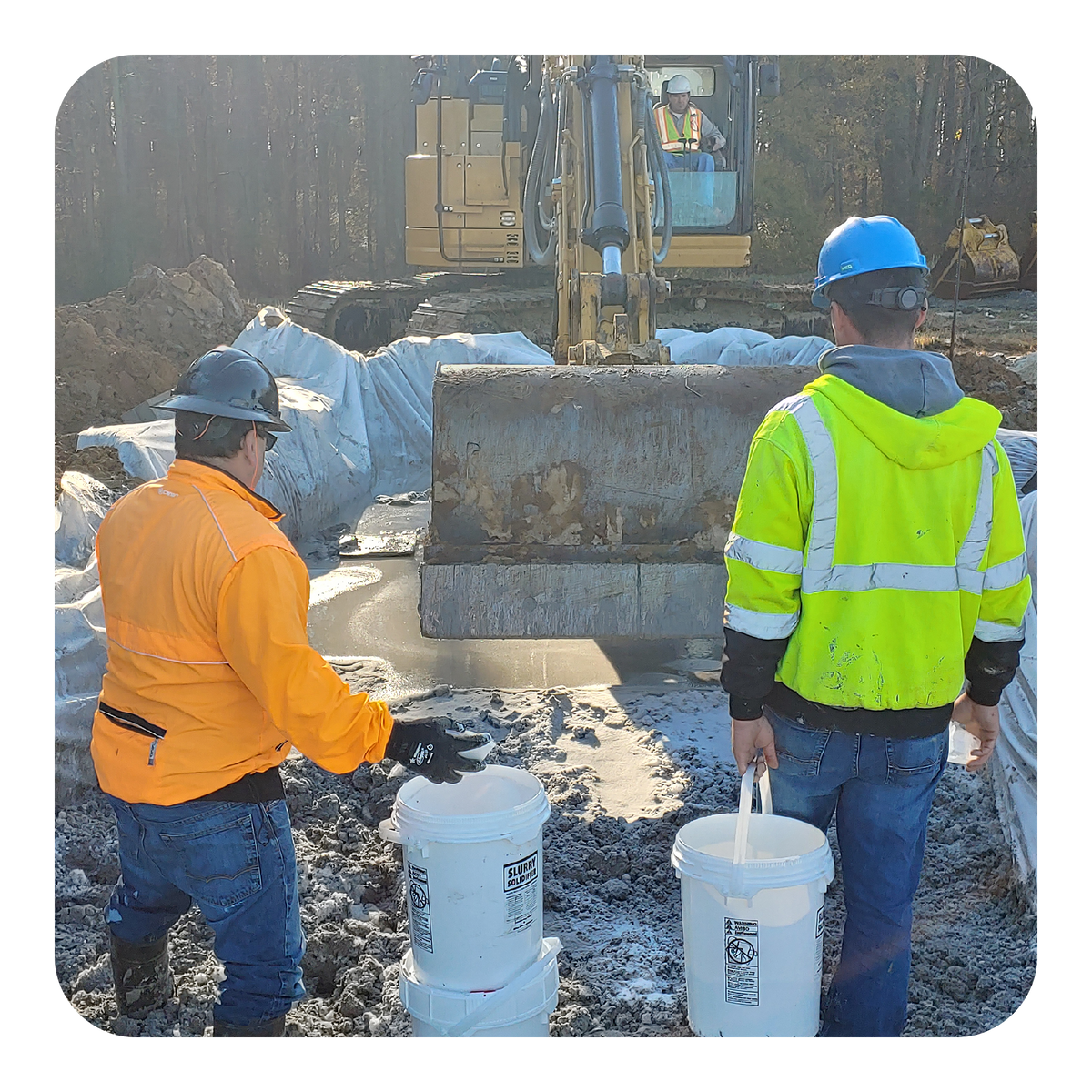 Two workers at a construction site with an excavator in the background.