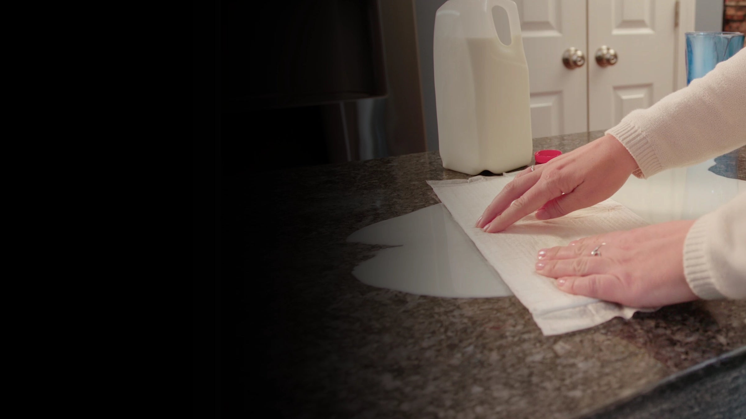 Person cleaning a countertop with a white Quick Dam Mat, with a milk jug in the background.