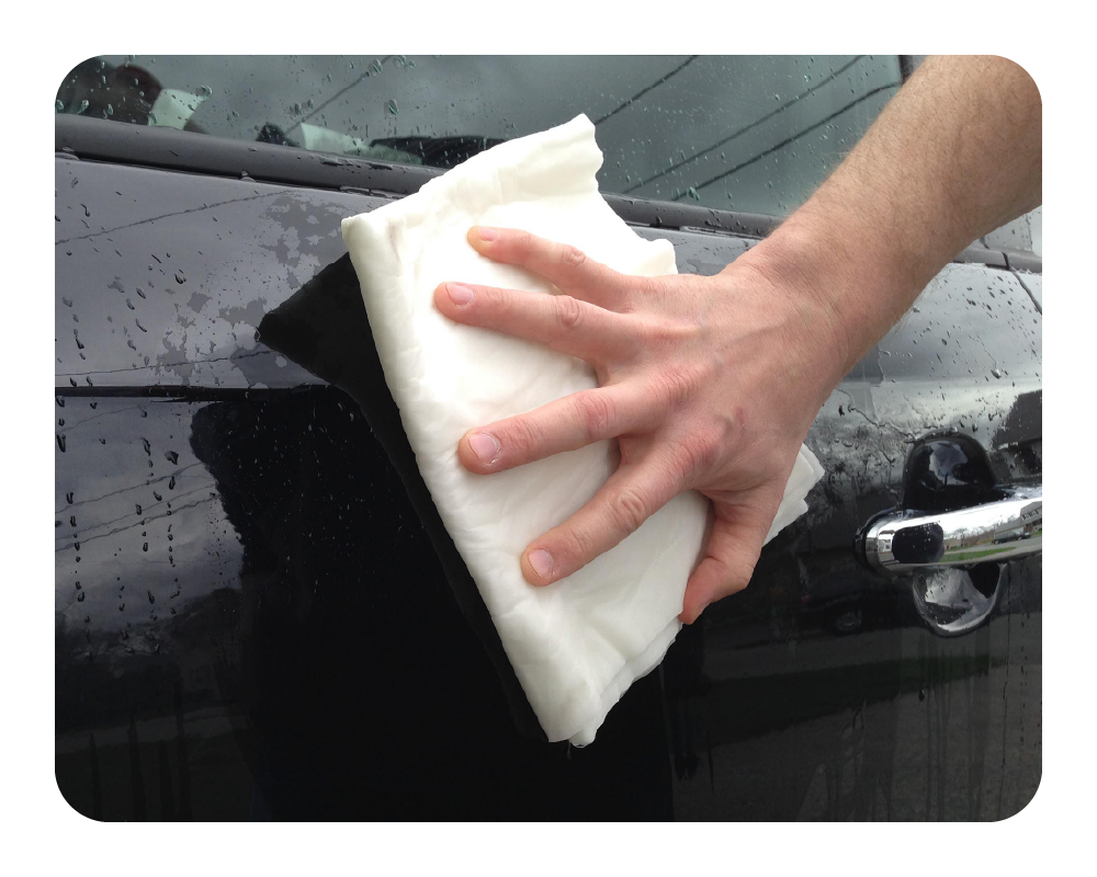 Person cleaning a car window with a white Quick Dam Mighty Mat